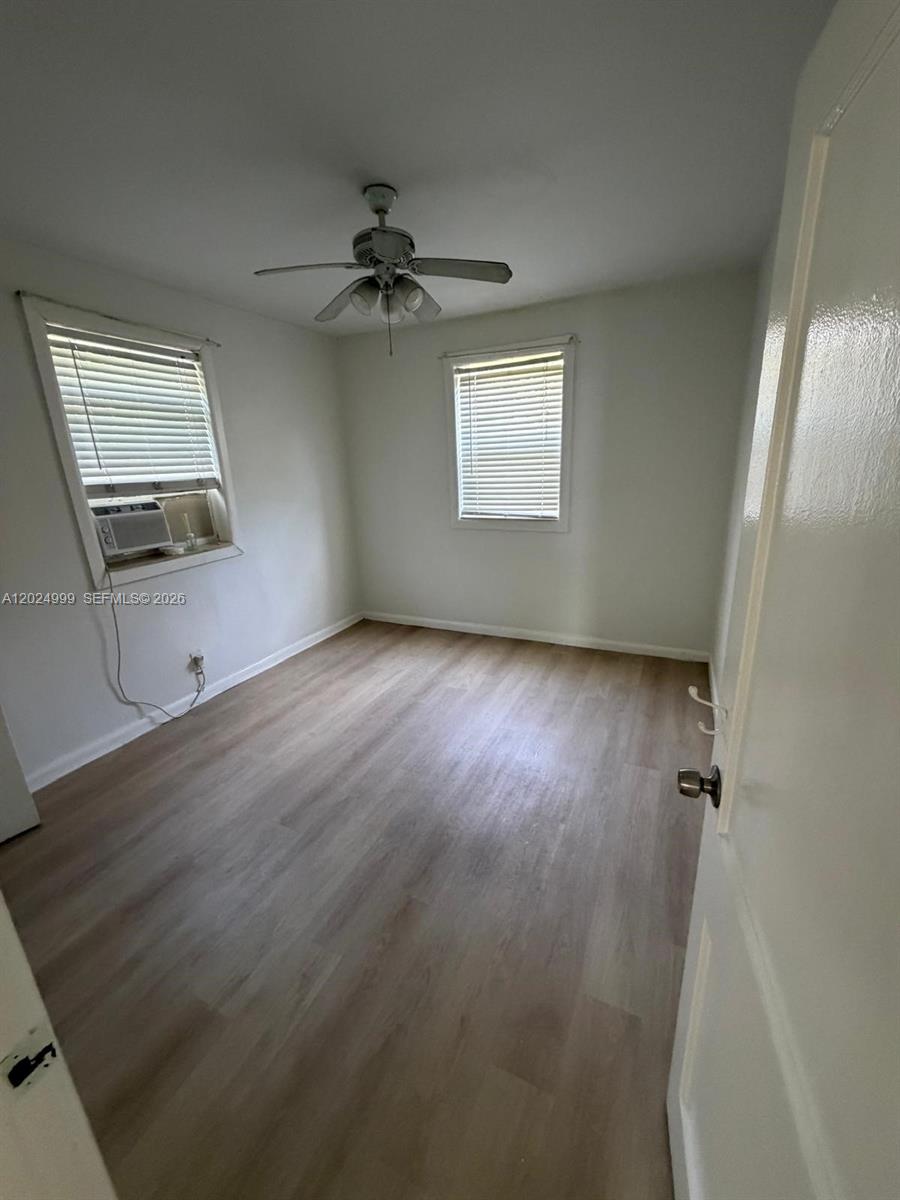 A bedroom with light wood-look flooring, white walls, a ceiling fan, and two windows — HOLLYWOOD, FL