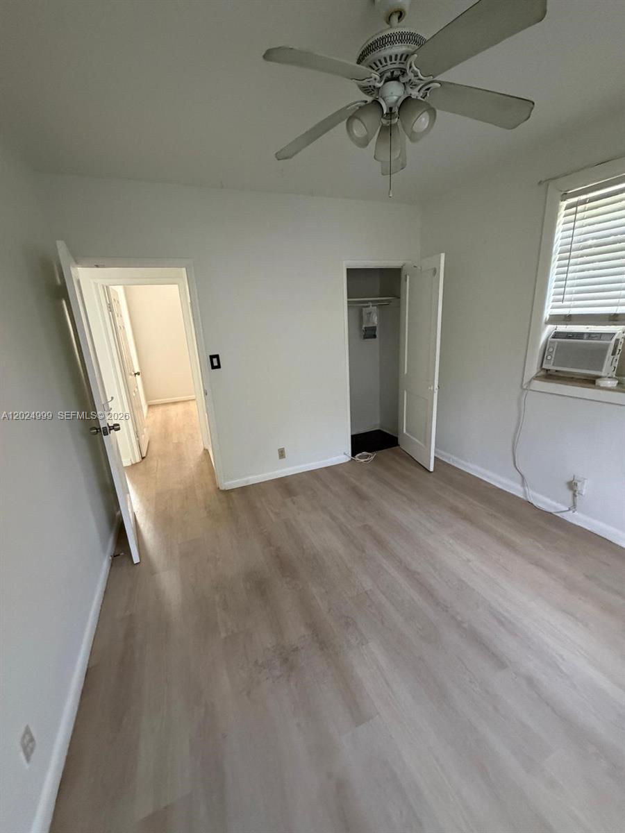 A bedroom features light wood-look flooring, a ceiling fan, a closet, and a window unit — HOLLYWOOD, FL