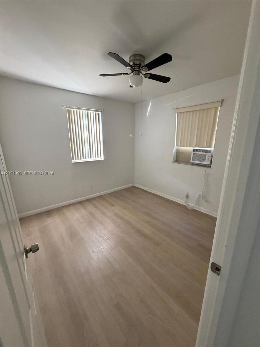 An empty bedroom features light wood-look flooring, white walls, a ceiling fan, and a window unit — HOLLYWOOD, FL