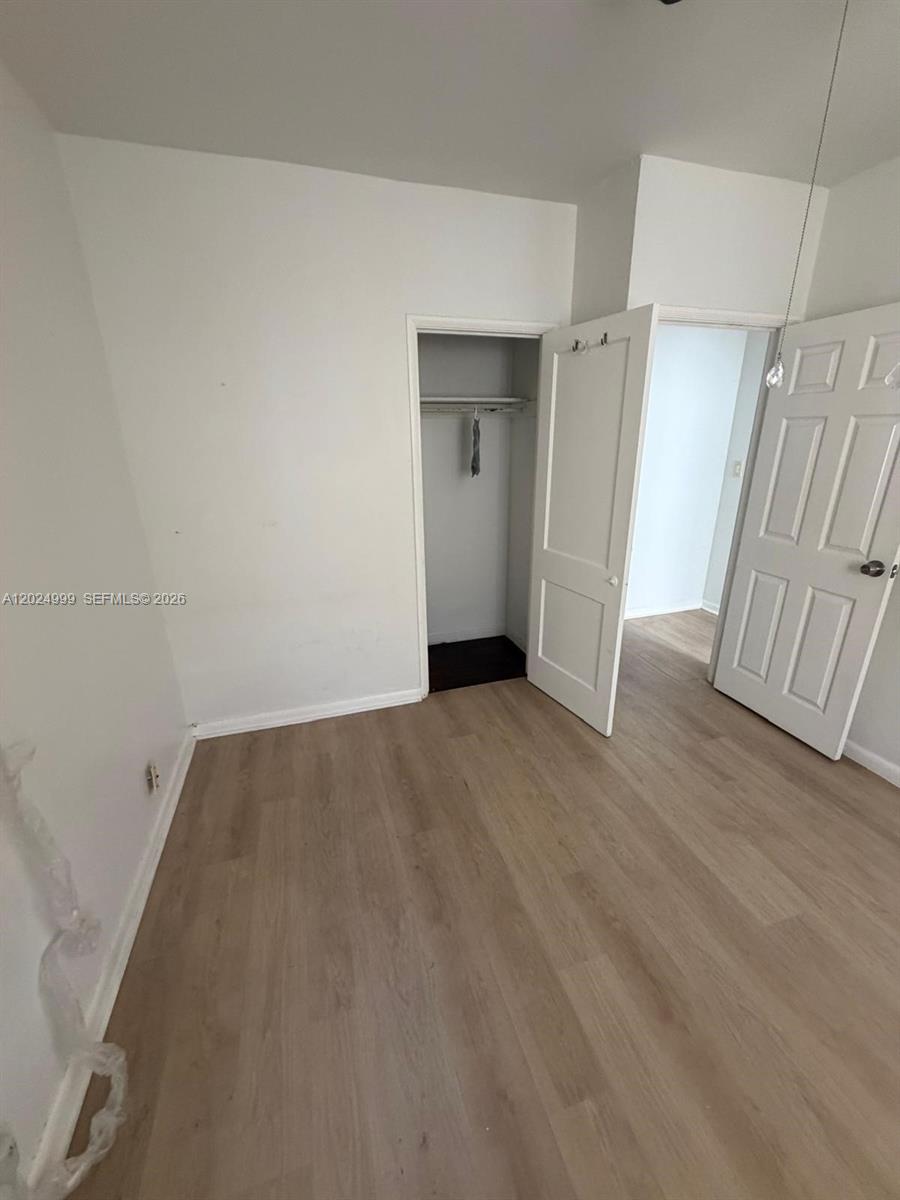 An empty room features light-colored wood-look flooring, white walls, and an open closet — HOLLYWOOD, FL