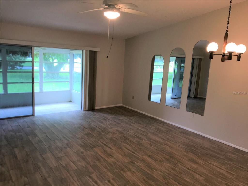 A living room with wood-look tile flooring, a ceiling fan, and three arched wall mirrors — 3705 34TH AVE DRIVE W, BRADENTON, FL