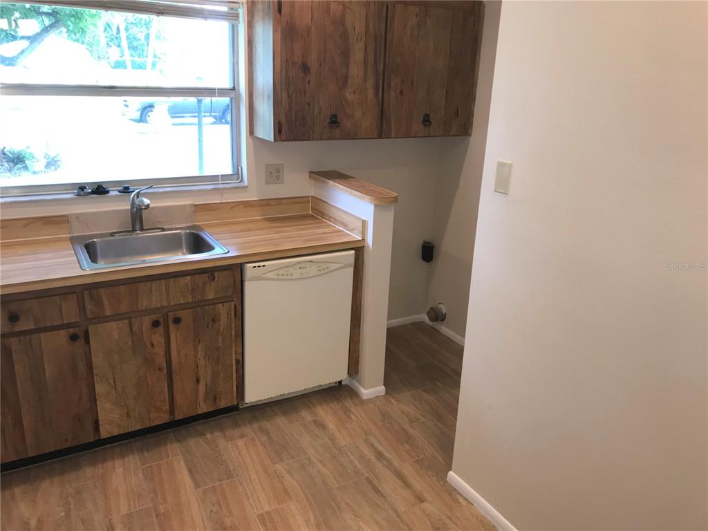 A kitchen features wood-grain cabinets, a stainless steel sink, and a white dishwasher — 3705 34TH AVE DRIVE W, BRADENTON, FL