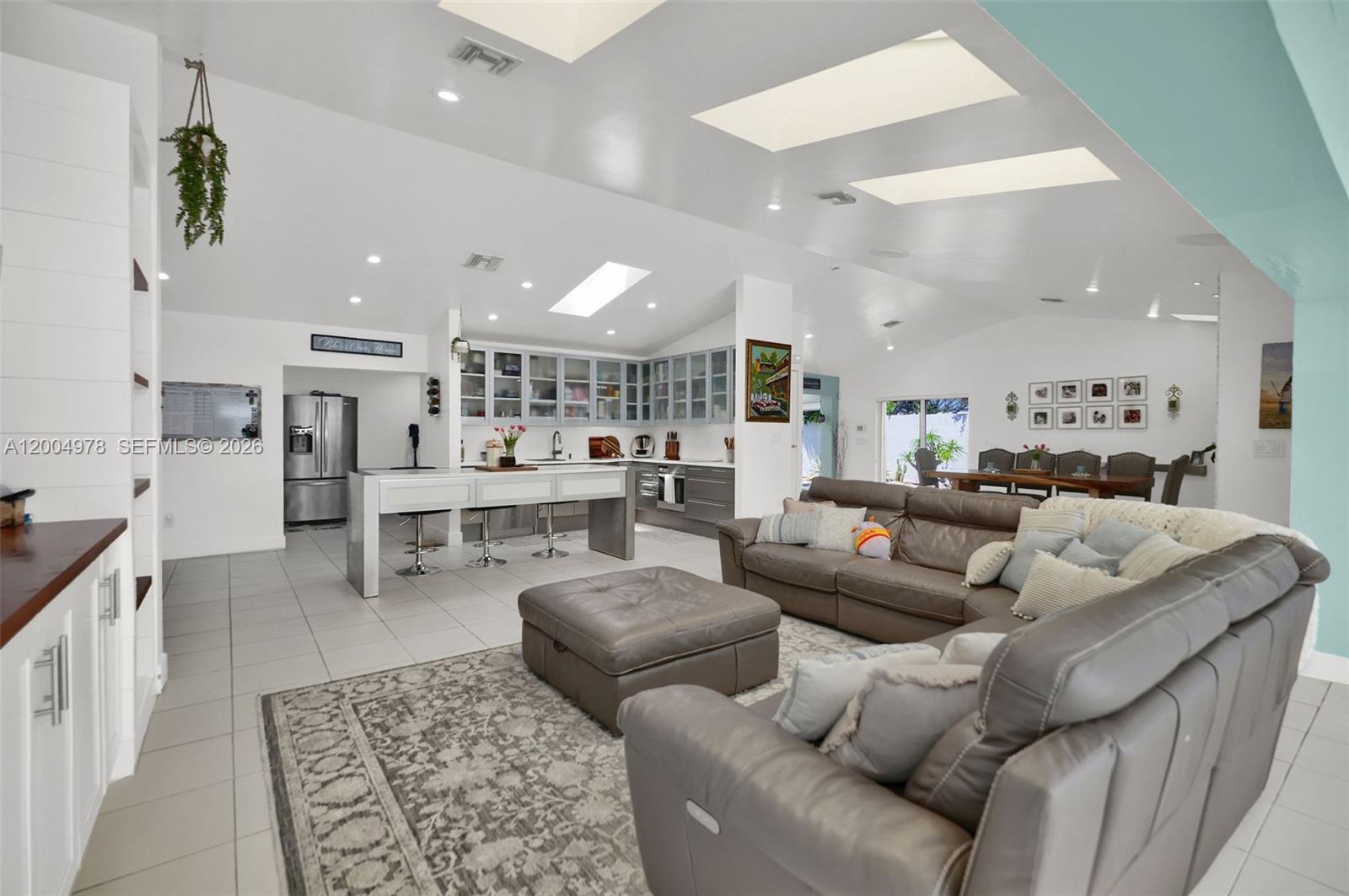 A spacious open-concept living room and kitchen featuring tile floors, skylights, and gray furniture — 15540 SW 152nd Ter, Miami FL 33187, MIAMI, FL