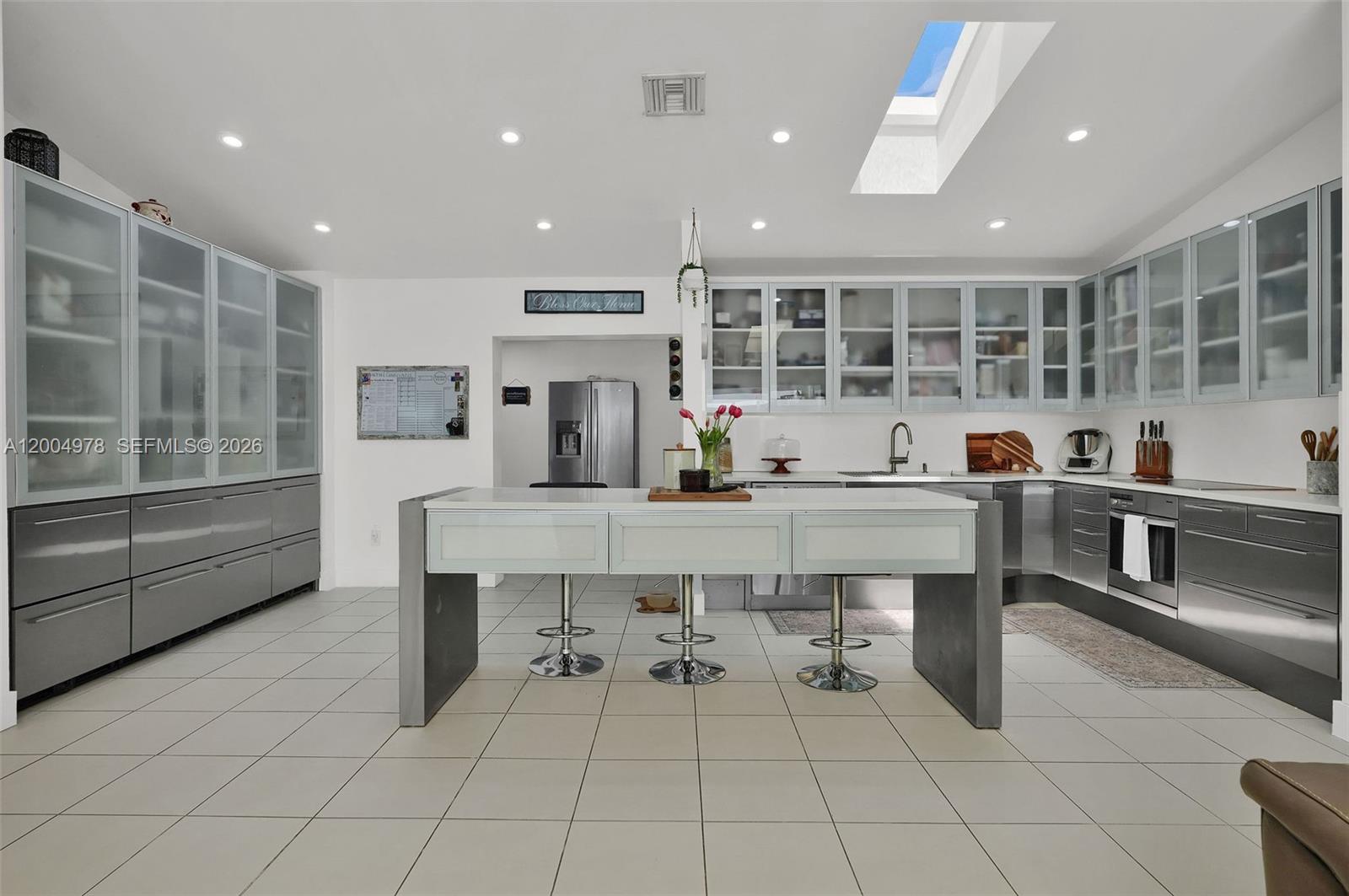 A modern kitchen features gray cabinetry, a central island with bar stools, and a skylight — 15540 SW 152nd Ter, Miami FL 33187, MIAMI, FL