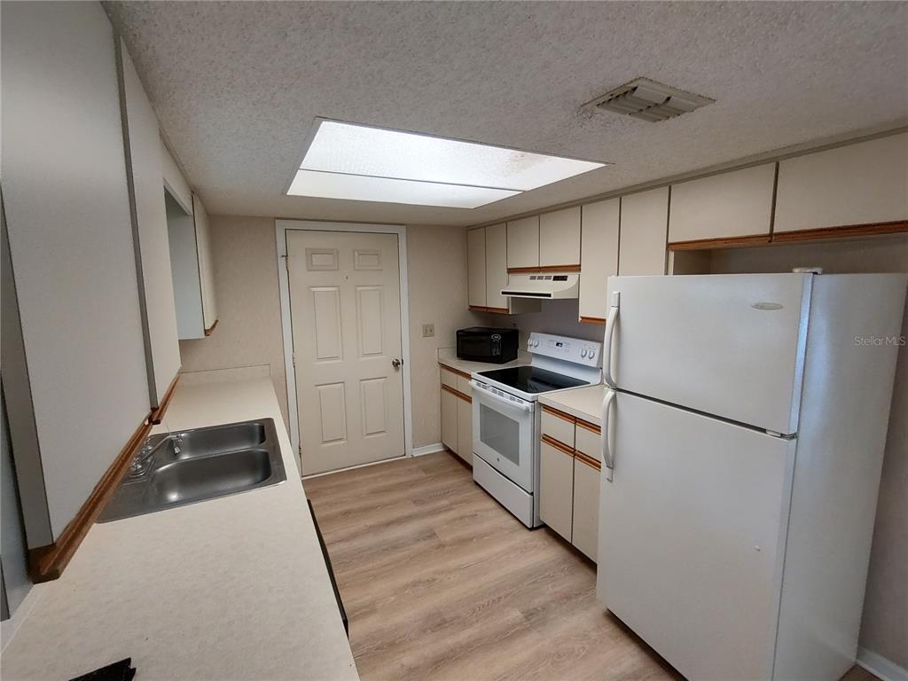 A kitchen features white appliances, light-colored cabinets, a double sink, and wood-look flooring — 6345 SW 115TH STREET ROAD, OCALA, FL