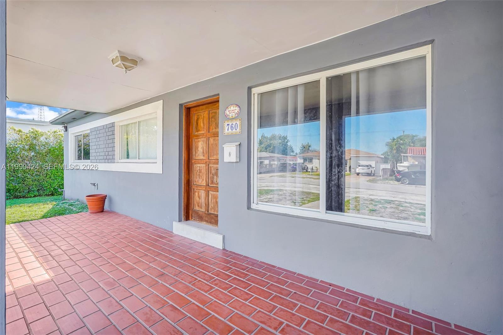 A covered porch with red tile flooring leads to a wooden front door — 760 E 55th St, Hialeah FL 33013, HIALEAH, FL