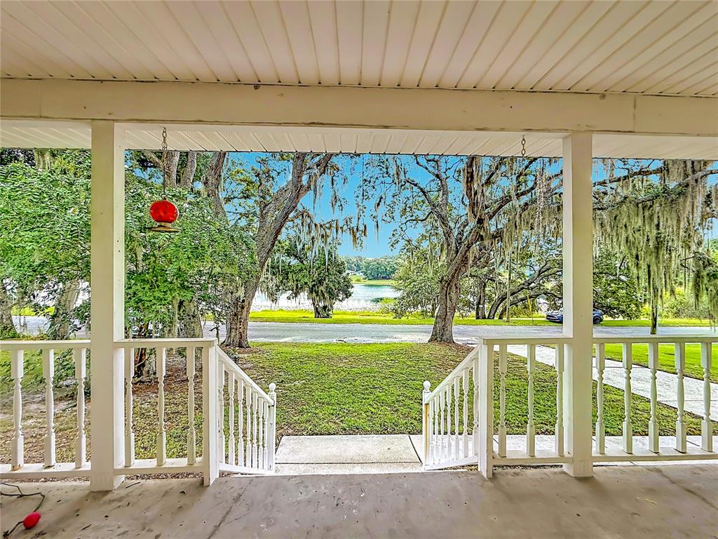 A covered porch with white railings overlooks a grassy yard, trees, and a distant lake — 540 DREW AVENUE, CLERMONT, FL