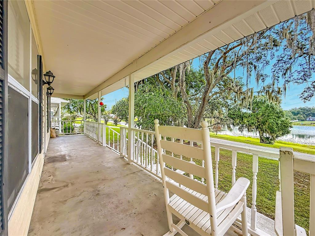 A covered porch features a white rocking chair, a railing, and a view of a lake — 540 DREW AVENUE, CLERMONT, FL