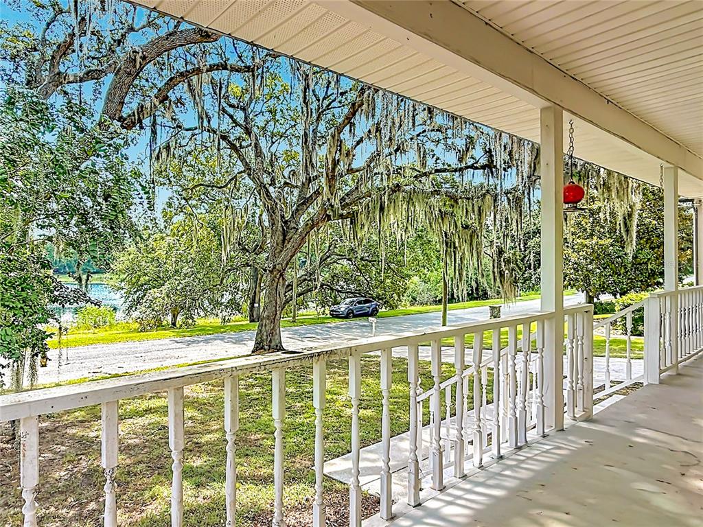 A covered porch with a white railing overlooks a tree-lined street and a body of water — 540 DREW AVENUE, CLERMONT, FL