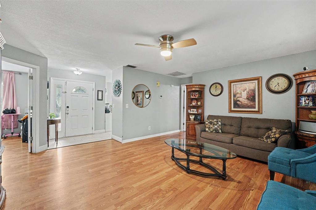 A living room features light gray walls, wood-look flooring, a ceiling fan, and brown furniture — 818 CAMBRIDGE WAY, LAKE WALES, FL