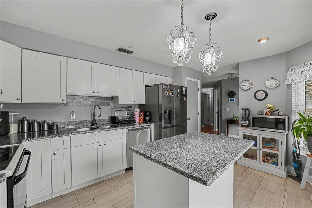 A kitchen features white cabinets, granite countertops, a center island, and two crystal pendant lights — 818 CAMBRIDGE WAY, LAKE WALES, FL