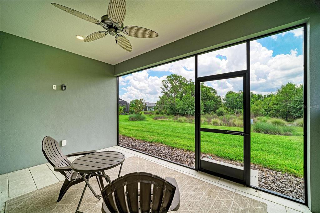 A screened-in patio features a ceiling fan, outdoor furniture, and a view of green space — 1047 WATERLINE COURT, SARASOTA, FL