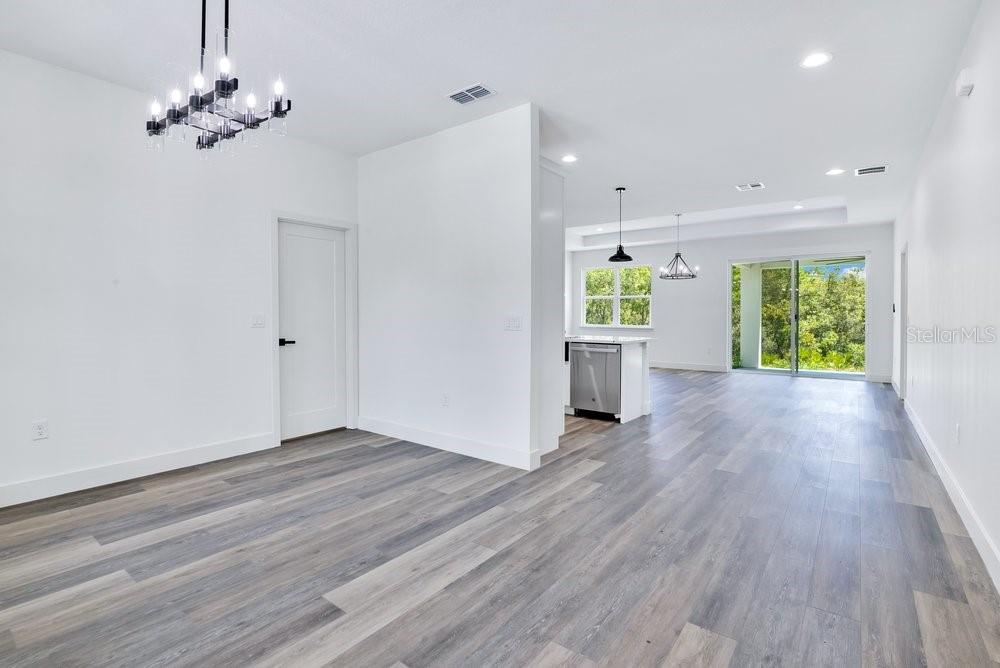 An open-concept living and kitchen area with light wood-look flooring and a modern chandelier — 41824 ASPEN STREET, EUSTIS, FL