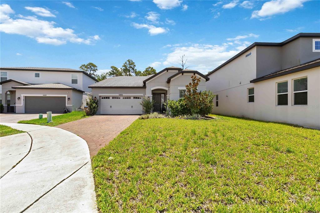 A single-story house with a brick driveway and a front lawn under a blue sky — 5456 CARRARA COURT, ST CLOUD, FL