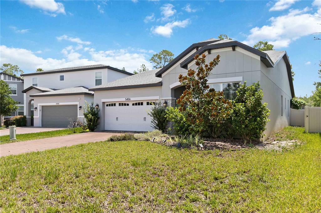 A single-story house with a two-car garage and a large magnolia tree in front — 5456 CARRARA COURT, ST CLOUD, FL