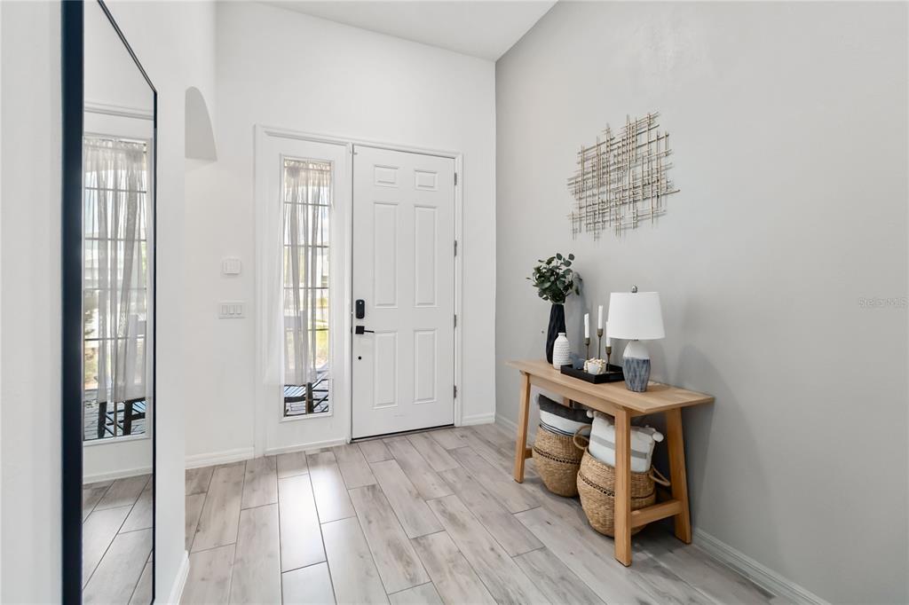 A bright entryway features light wood-look tile flooring, a white front door, and a console table — 5456 CARRARA COURT, ST CLOUD, FL