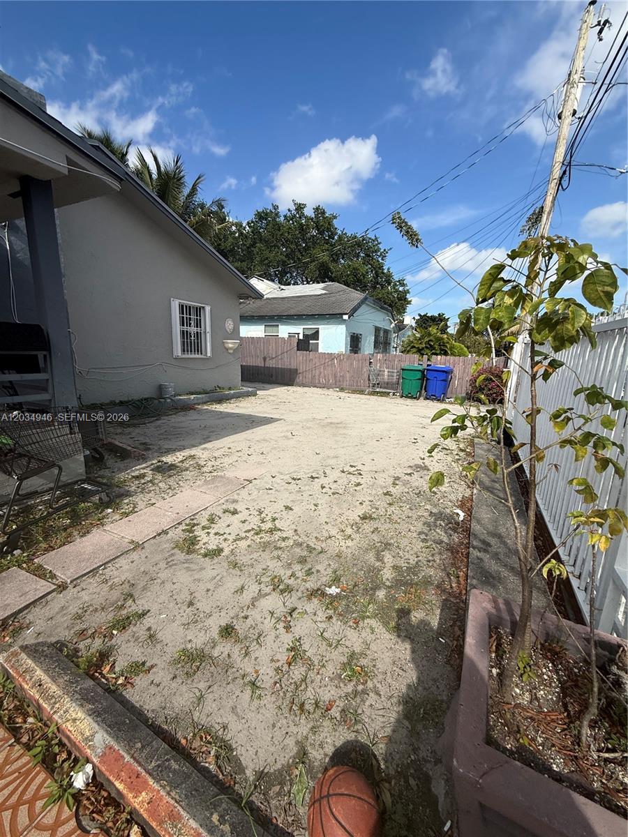 A sandy side yard features a gray house, a wooden fence, and two trash bins — 1143 NW 27th St, Miami FL 33127, MIAMI, FL