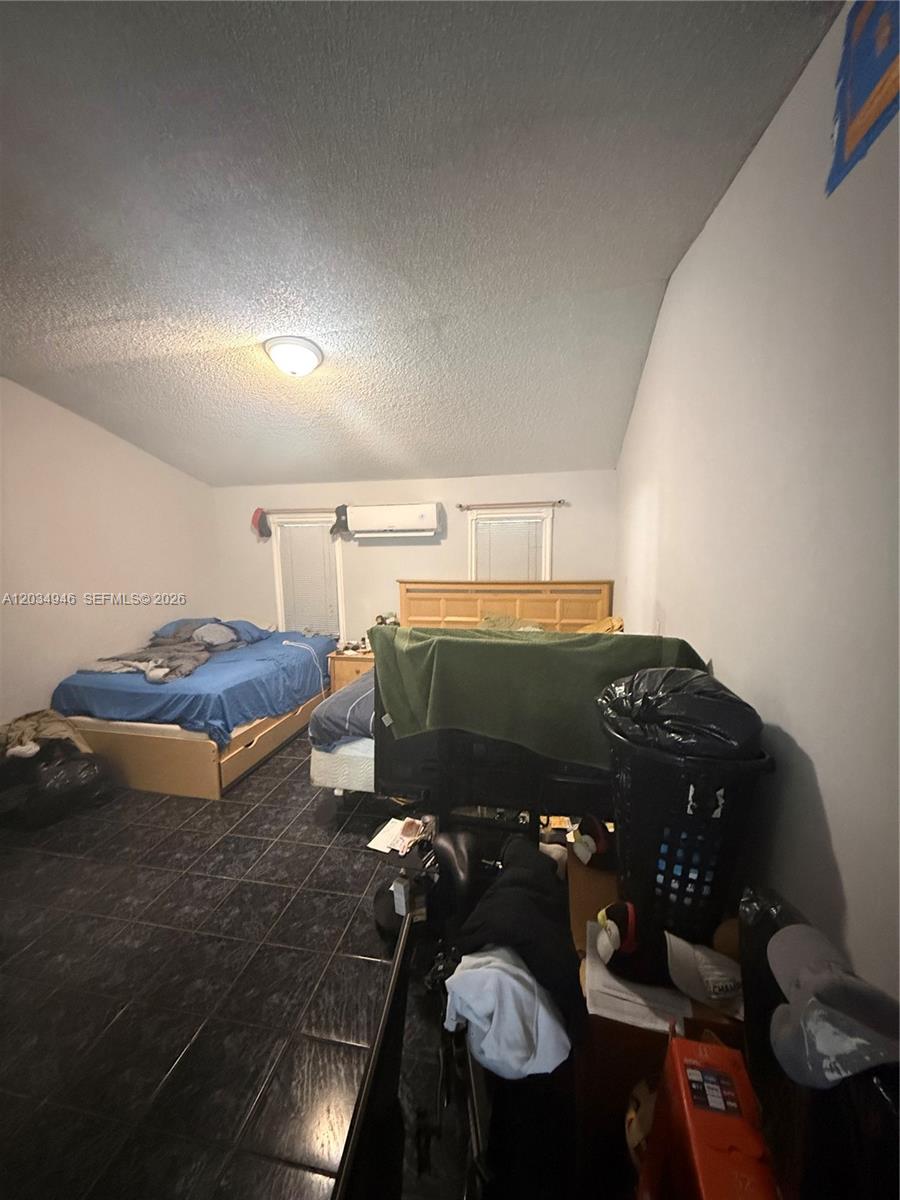 A bedroom with dark tile flooring, two beds, and a wall-mounted air conditioning unit — 1143 NW 27th St, Miami FL 33127, MIAMI, FL