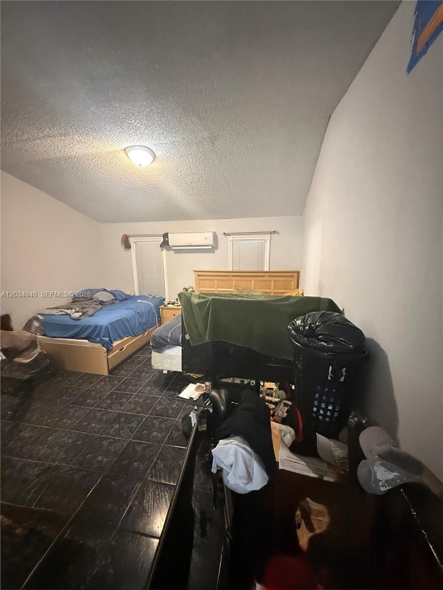 A bedroom features dark tile flooring, two beds, and a wall-mounted air conditioning unit — 1143 NW 27th St, Miami FL 33127, MIAMI, FL