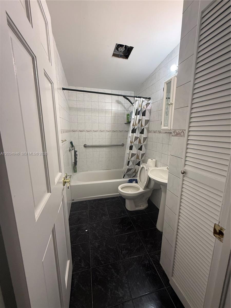 A bathroom features a bathtub with a shower curtain, a toilet, and a pedestal sink — 1143 NW 27th St, Miami FL 33127, MIAMI, FL