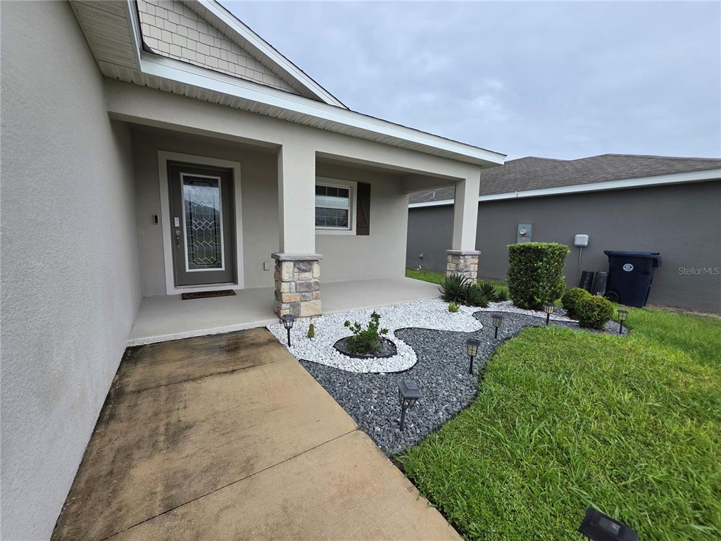A covered front porch features stone-accented columns, a glass-paneled door, and a decorative rock garden — 424 CAPRI WAY, AUBURNDALE, FL