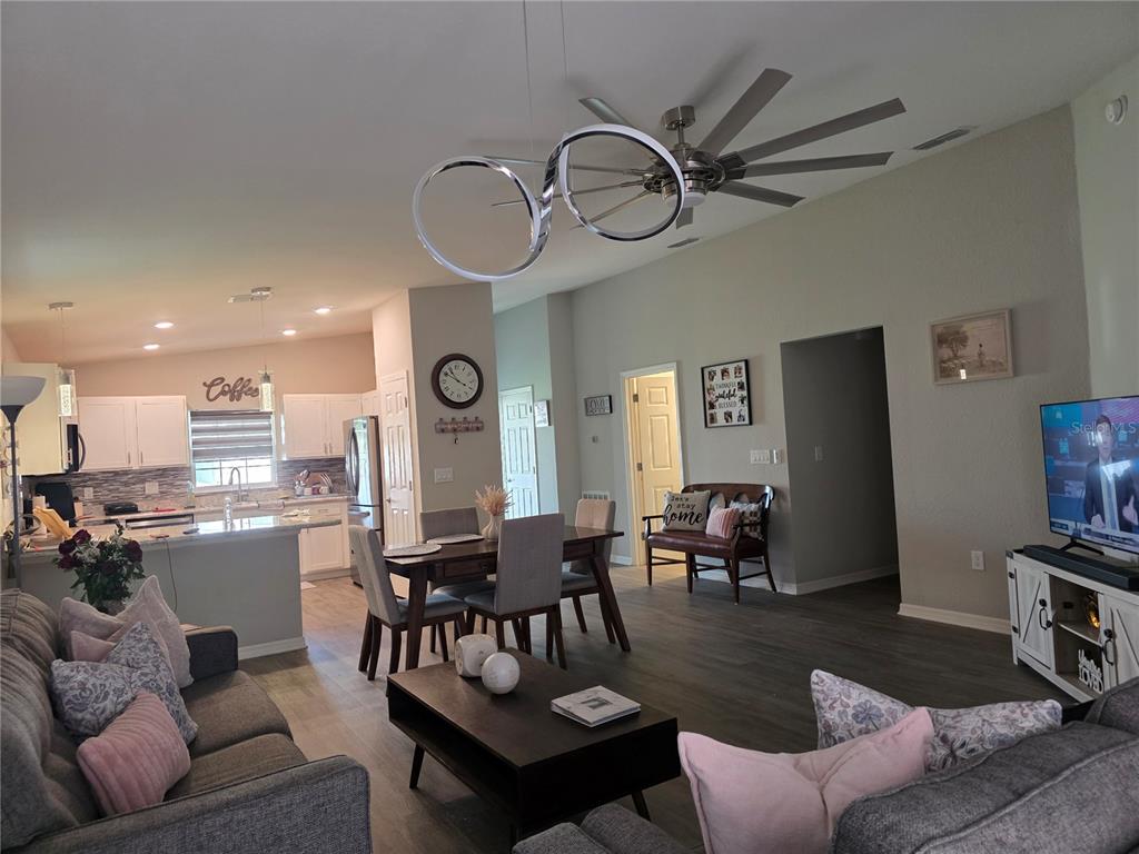 An open-concept living room and kitchen featuring gray flooring, a modern light fixture, and furniture — 424 CAPRI WAY, AUBURNDALE, FL