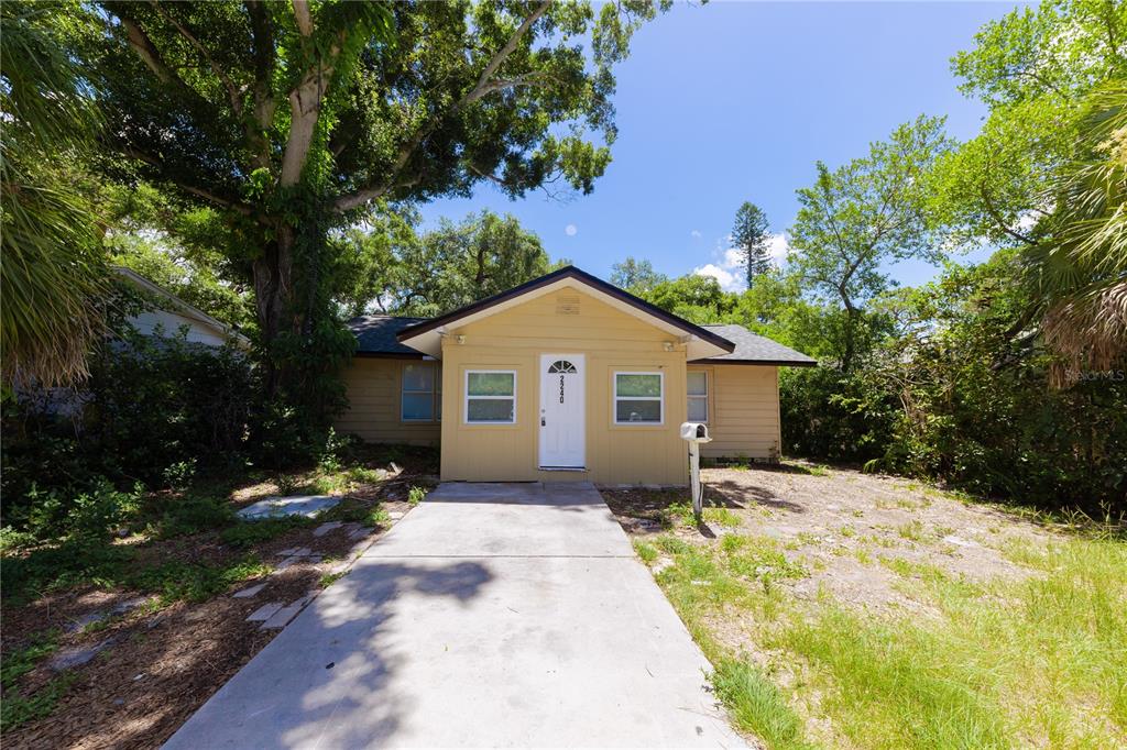 A yellow, single-story house with a concrete driveway and surrounding trees under a blue sky — 2240 10TH STREET S, ST PETERSBURG, FL