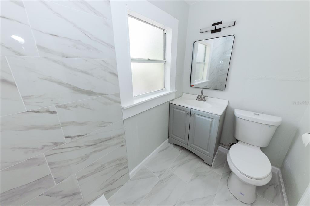 A bathroom features marble-look tile flooring and shower walls, a gray vanity, and a toilet — 2240 10TH STREET S, ST PETERSBURG, FL