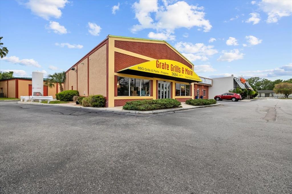 A commercial building with a red brick facade and a yellow awning labeled Grate Grills — 3684 TAMPA ROAD UNIT 101, OLDSMAR, FL