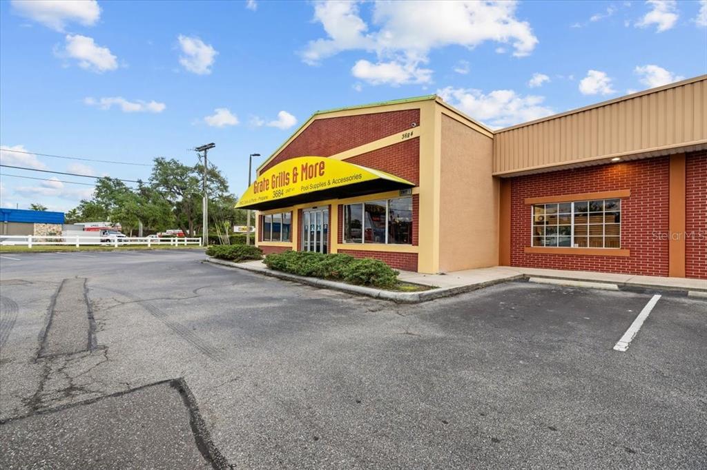 A brick commercial building with a yellow awning and parking lot under a blue sky — 3684 TAMPA ROAD UNIT 101, OLDSMAR, FL