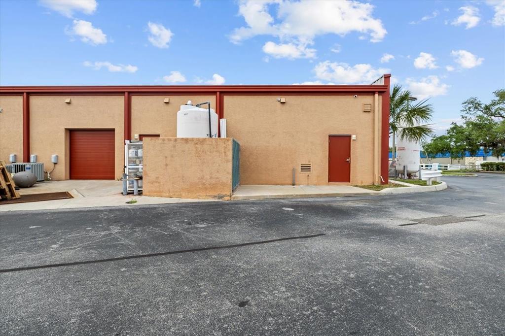 The exterior of a commercial building features a roll-up door, a side door, and equipment — 3684 TAMPA ROAD UNIT 101, OLDSMAR, FL