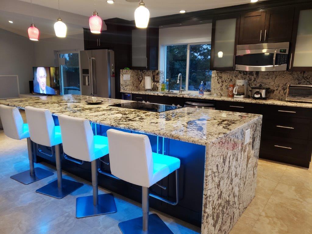 A modern kitchen features a large granite island with blue under-cabinet lighting and white barstools — 801 NW 49th Way, Coconut Creek FL 33063, COCONUT CREEK, FL