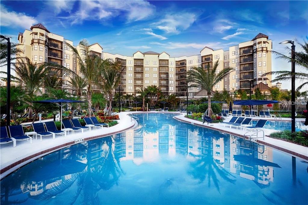 A large swimming pool sits in front of a multi-story apartment building with palm trees — 14501 GROVE RESORT AVENUE UNIT 3205, WINTER GARDEN, FL