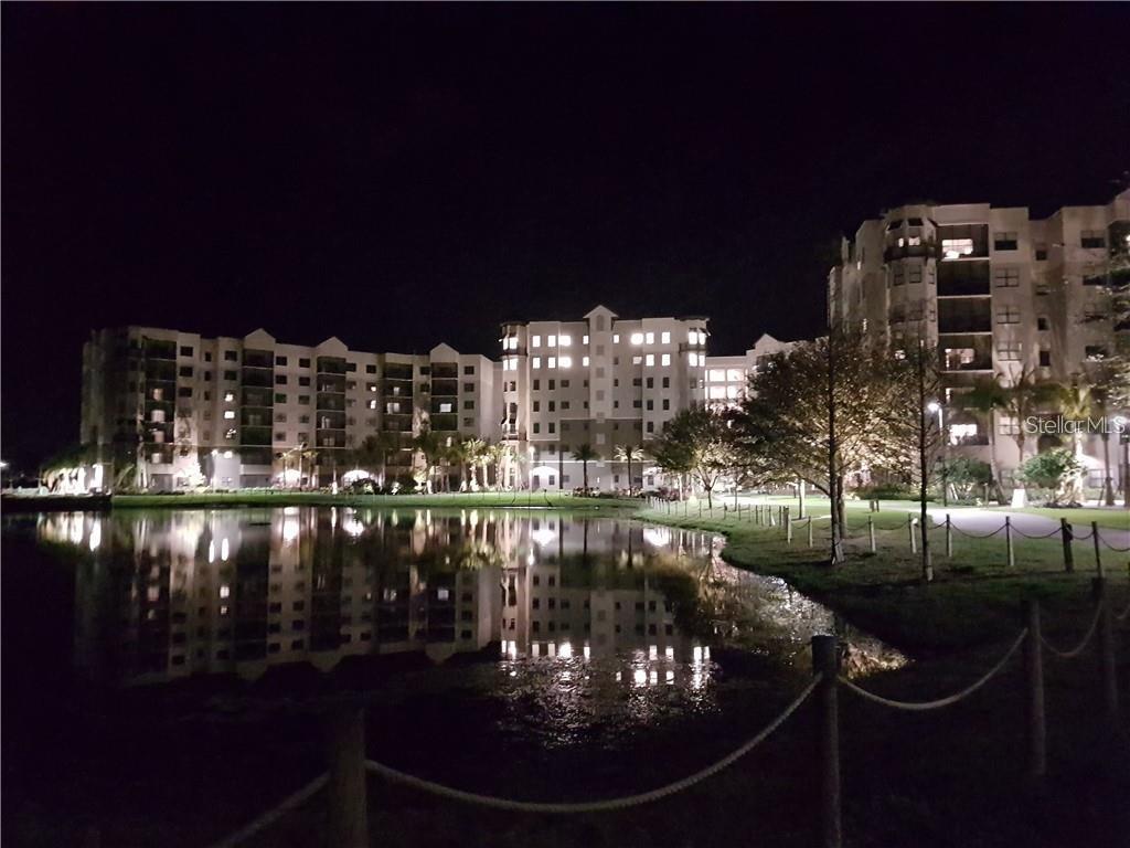 A multi-story apartment building is illuminated at night beside a reflective pond — 14501 GROVE RESORT AVENUE UNIT 3205, WINTER GARDEN, FL
