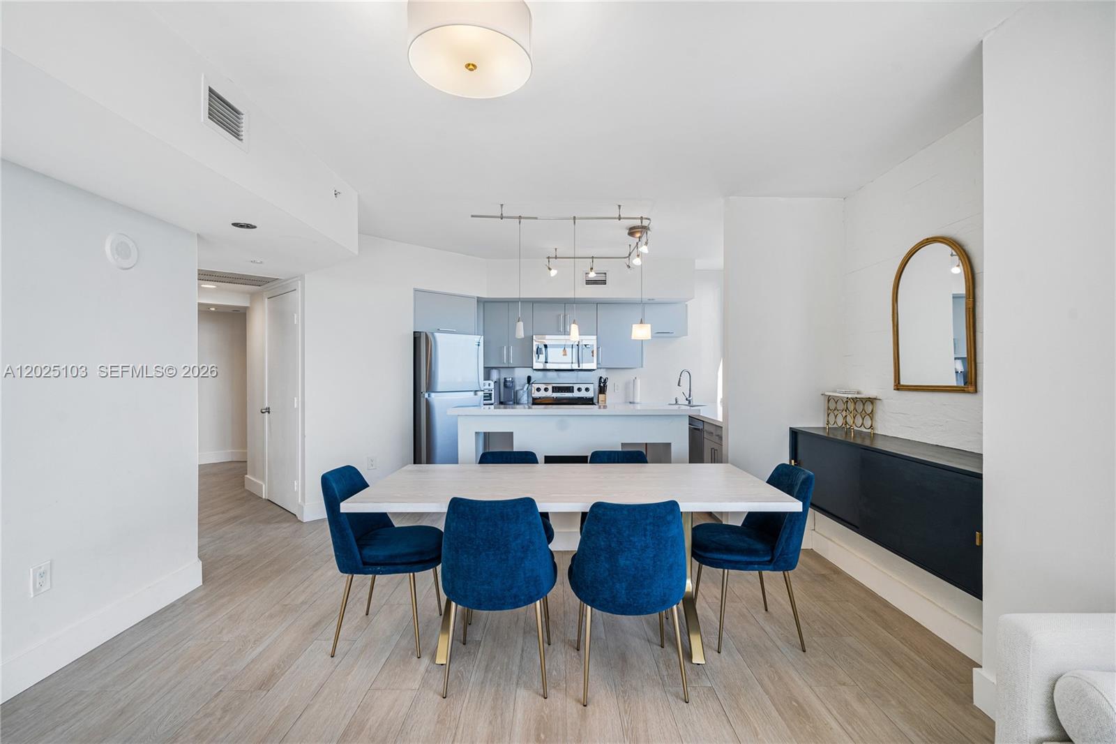 A dining area with a white table and blue chairs sits before an open kitchen — 1330 West Ave # 2107, Miami Beach FL 33139, MIAMI BEACH, FL