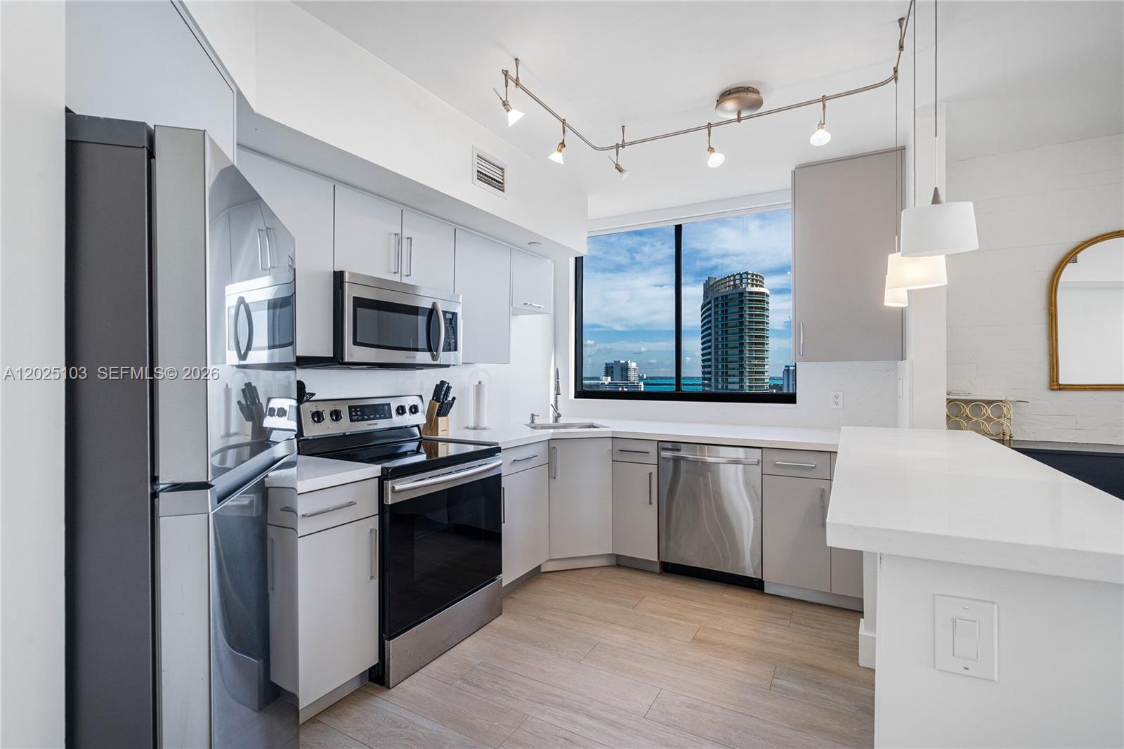 A modern kitchen features stainless steel appliances, white cabinetry, and a view of a skyscraper — 1330 West Ave # 2107, Miami Beach FL 33139, MIAMI BEACH, FL
