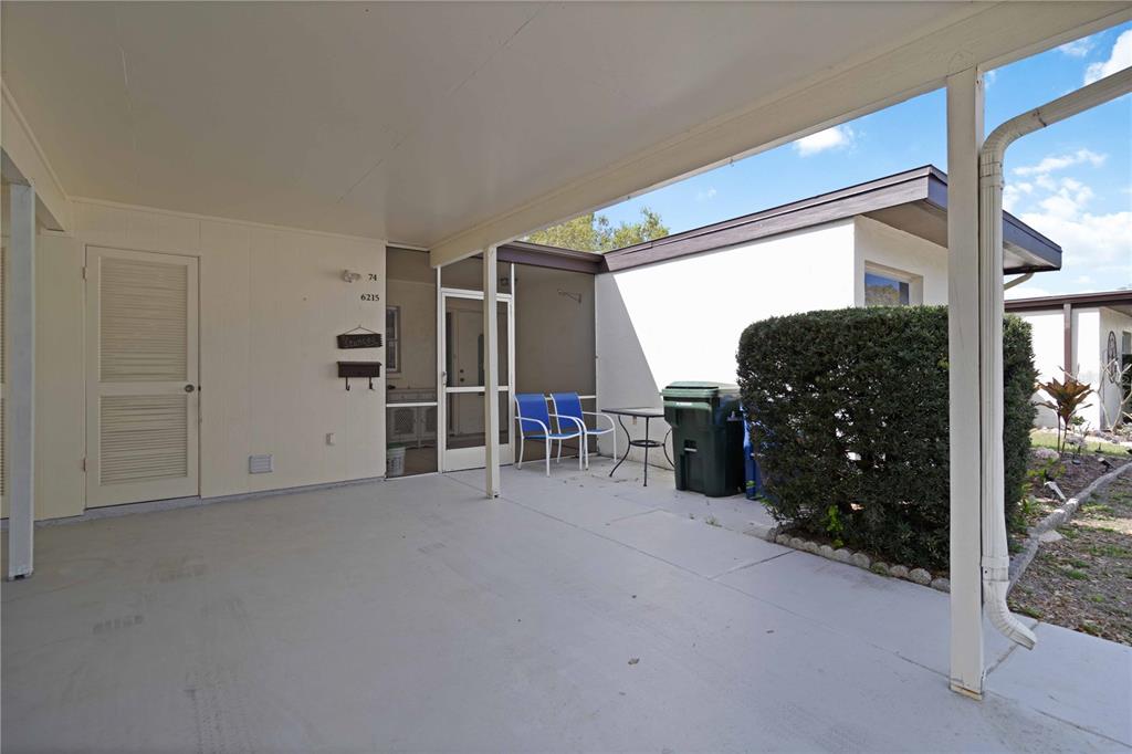 A covered concrete patio features a white door, a screened entryway, and outdoor seating — 6215 GREEN VIEW CIRCLE UNIT 74, SARASOTA, FL