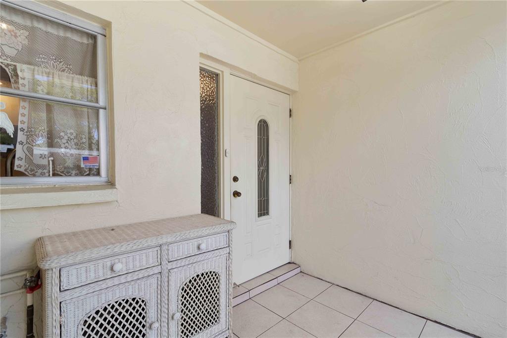 A white front door with a side light sits on a tiled porch with furniture — 6215 GREEN VIEW CIRCLE UNIT 74, SARASOTA, FL