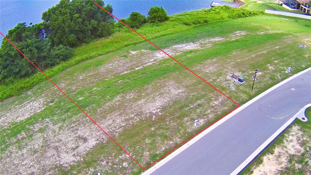 An aerial view shows a vacant, grassy residential lot bordered by a road and water — 4383 JULIANA LAKE DRIVE, AUBURNDALE, FL