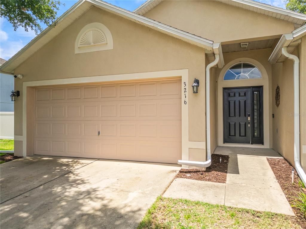The exterior of a beige house features a two-car garage and a dark front door — 3216 PARK BRANCH AVENUE, CLERMONT, FL