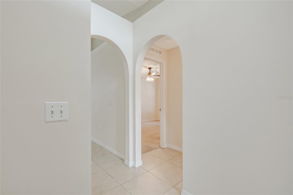 A hallway with arched doorways leads to a room with a ceiling fan and carpet — 3216 PARK BRANCH AVENUE, CLERMONT, FL