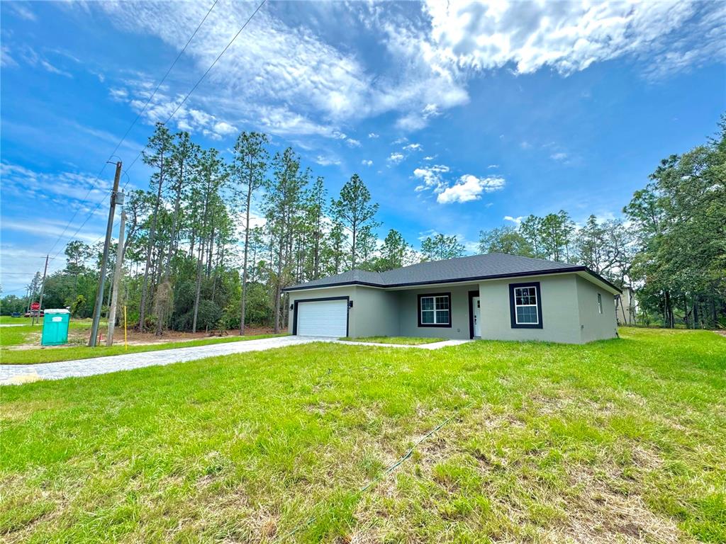 A single-story house with a garage and light green exterior sits on a grassy lot — 11032 N TRIGGER TERRACE, CITRUS SPRINGS, FL