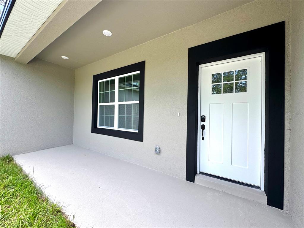 A covered concrete porch features a white front door and a window with black trim — 11032 N TRIGGER TERRACE, CITRUS SPRINGS, FL