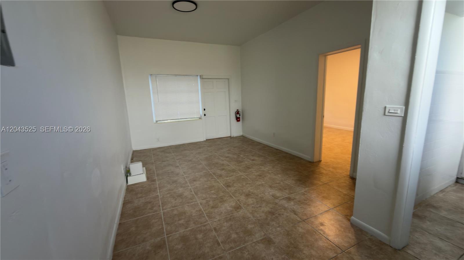An empty room features beige tile flooring, white walls, a window, and a doorway — 808 84th St # 812, Miami Beach FL 33141, MIAMI BEACH, FL