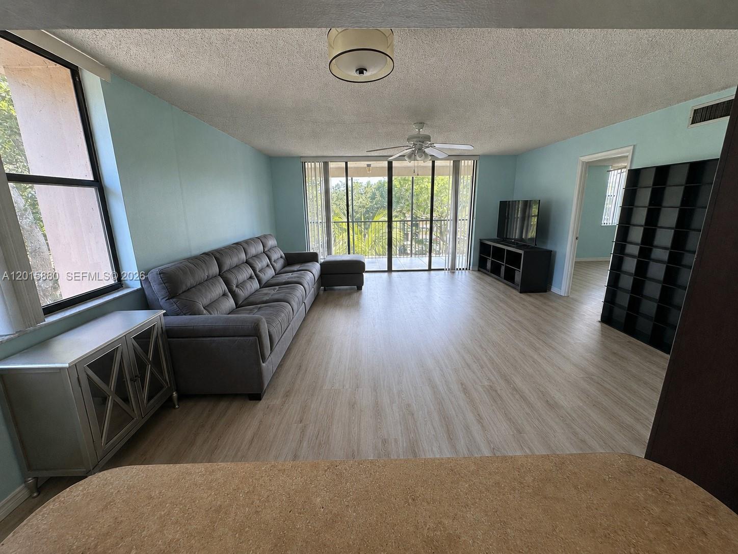 A living room features light blue walls, wood-look flooring, a gray sofa, and a balcony — 6800 Cypress Rd # 415, Plantation FL 33317, PLANTATION, FL