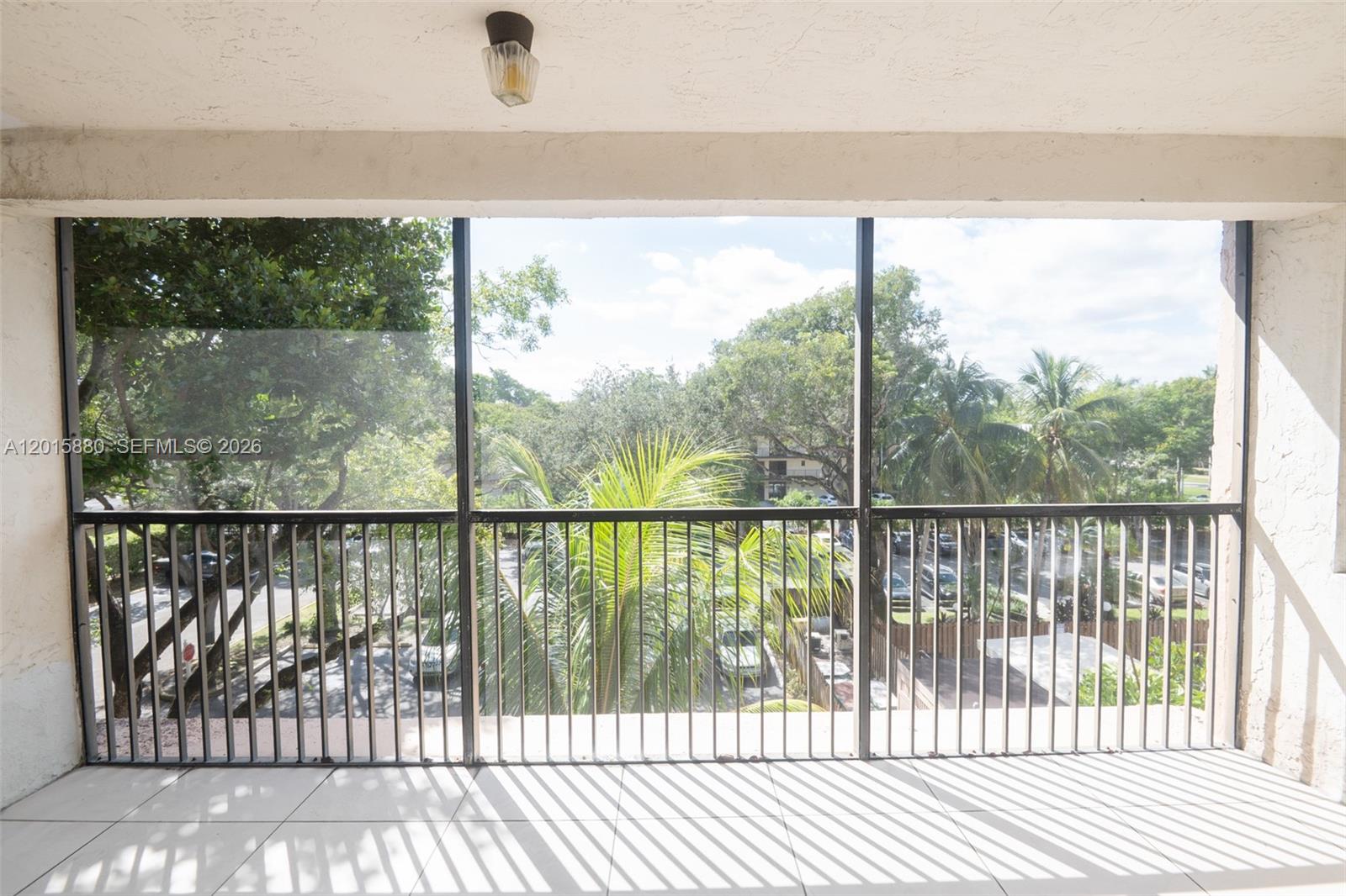 A screened-in balcony features white tiled flooring, a ceiling light, and views of trees — 6800 Cypress Rd # 415, Plantation FL 33317, PLANTATION, FL
