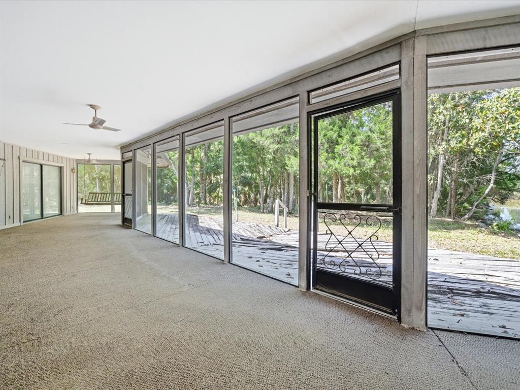 A screened-in porch with carpeted flooring overlooks a wooden deck and wooded yard — 8979 W WHITE DOGWOOD DRIVE, HOMOSASSA, FL