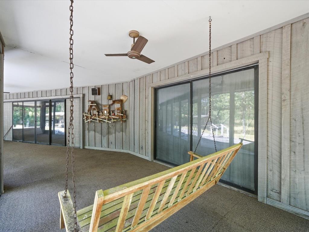 A covered patio features a wooden porch swing, gray wood siding, and sliding glass doors — 8979 W WHITE DOGWOOD DRIVE, HOMOSASSA, FL