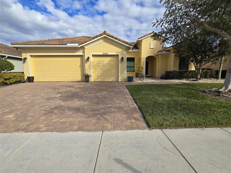A yellow single-story house features a three-car garage, a paver driveway, and a front lawn — 2095 NW Diamond Creek Way, Jensen Beach FL 34957, JENSEN BEACH, FL