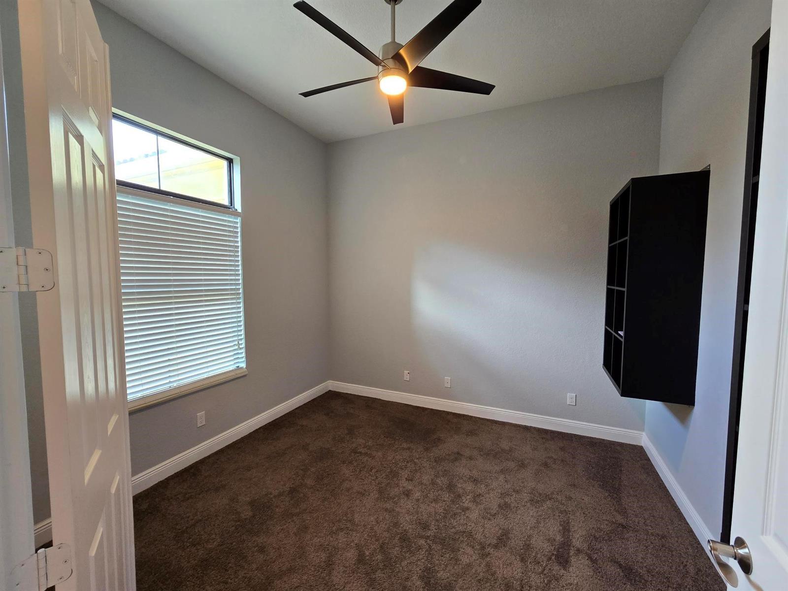 An empty bedroom features gray walls, brown carpet, a ceiling fan, and a wall-mounted shelf — 2095 NW Diamond Creek Way, Jensen Beach FL 34957, JENSEN BEACH, FL